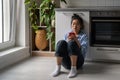 Upset gloomy young Asian woman looking at mobile phone screen feeling sad while sitting on floor Royalty Free Stock Photo
