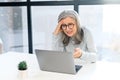 Upset gray-haired senior woman looking at laptop screen sitting at desk in office Royalty Free Stock Photo