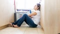 Upset young housewife sittting on floor at laundry