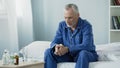 Upset ill senior male sitting on bed, taking medication to recover from illness Royalty Free Stock Photo