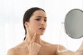 Upset Indian woman holding magnifying mirror and looking at pimple on chin Royalty Free Stock Photo