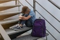Upset little boy with backpack sitting on stairs indoors Royalty Free Stock Photo
