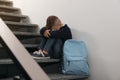 Upset little boy with backpack sitting on stairs indoors Royalty Free Stock Photo