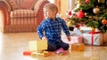 Upset little boy sitting on floor and holding Christmas gift