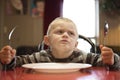 A Upset little boy waiting for dinner while holding a fork and a spoon Royalty Free Stock Photo