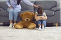 Upset little girl crying on floor near teddy bear while mother comforting her at home. Parent soothing her unhappy child Royalty Free Stock Photo