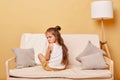 Upset little girl sitting backwards on couch at home, depressed female child having bad mood, offended kid feeling sadness, Royalty Free Stock Photo