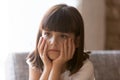 Upset little girl sitting on couch at home feels unhappy