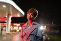 Upset lonely young millennial woman standing near petrol station shop in red neon light at night