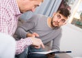 Upset man with friend looking at papers on sofa Royalty Free Stock Photo