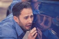 Upset man looking at scratches and dents on his car outdoors