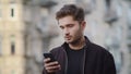 Upset man using phone outside. Annoyed guy looking screen on street.