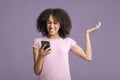 Upset millennial african american lady in pink t-shirt with curly hair, reads message and gets angry