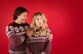 Upset millennial girl in Christmas outfit and boyfriend comforting her on red background, free space