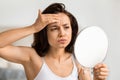 Upset millennial woman looking at mirror, checking pimple Royalty Free Stock Photo