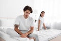 Upset offended caucasian young male ignoring female sitting in bed in white bedroom interior, lady apologizes