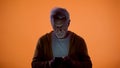 Upset old man typing message on smartphone, orange background, vision problem