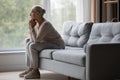 Upset older woman sit on sofa looking out window