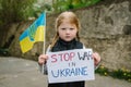 Upset poor toddler girl kid protesting war conflict raises banner with inscription message text Stop war in Ukraine and blue-
