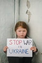 Upset poor toddler girl kid protesting war conflict raises banner with inscription text Stop war in Ukraine. Child sits near old