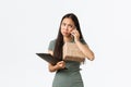 Upset pouting asian businesswoman holding clients package and clipboard with customer info, manage small business from Royalty Free Stock Photo