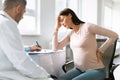 Upset pregnant woman suffering headache and lower back pain during meeting with her gynecologist male doctor in clinic Royalty Free Stock Photo