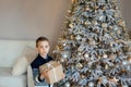 Upset preschooler Caucasian kid with present box in his hands near the Christmas tree. Portrait of frustrated boy in