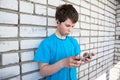 Upset preteen boy with smartphone and earphones, white brick wall Royalty Free Stock Photo