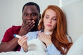 Upset redhaired ginger woman looking in pregnancy test with her african american boyfriend at home