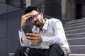 Upset and sad hindu businessman sitting on stairs outside office building, disappointed man reading online news using Royalty Free Stock Photo