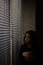 upset sad little girl sitting near window with blinds jalousie lit with warm light Royalty Free Stock Photo