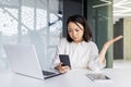 Upset sad woman at workplace holding smartphone, depressed business woman browsing social media inside office, Asian Royalty Free Stock Photo