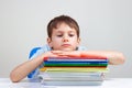 Upset schoolboy sitting at desk with pile of school books and notebooks