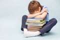 Upset schoolboy sitting with pile of school books and covers his face with hands. boy sleeping on a stack of textbooks Royalty Free Stock Photo