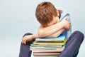 Upset schoolboy sitting with pile of school books and covers his face with hands. boy sleeping on a stack of textbooks Royalty Free Stock Photo