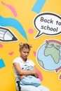 Upset schoolgirl holding backpack on chair