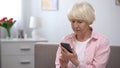 Upset senior female typing message on smartphone, missing family, loneliness