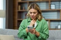 Upset senior woman sitting on sofa at home and holding phone. She looks worriedly at the screen, received a message, bad Royalty Free Stock Photo