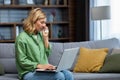 Upset senior woman sitting on sofa at home and looking at laptop. Sad, crying, wiping tears with a napkin Royalty Free Stock Photo