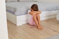 Upset small child girl crying sitting alone on floor, sitting near bed with her head down, sad lonely kid being bullied abused,