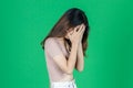 Upset stressed young Asian woman with hands on face feeling disappointed on green isolated background