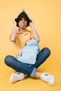 Upset teenager with backpack holding notebook above head on yellow background.