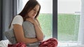 Upset thoughtful young woman in pajamas sitting on the bed and hugging a cushion tightly. Concept of depression, negative emotions Royalty Free Stock Photo