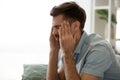 Upset tired man suffering from headache, touching temples close up