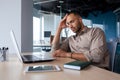 Upset tired young african american man sitting at desk with laptop in office, tired of work holding hand on head Royalty Free Stock Photo