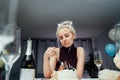 Upset, unhappy attractive woman eating festive cake while celebrating birthday at home, sitting alone at served table