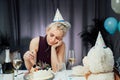 Upset, unhappy attractive woman eating festive cake while celebrating birthday at home, sitting alone at served table looking away