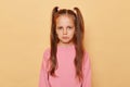 Upset unhappy little girl with ponytails wearing pink sweatshirt isolated over beige background looking at camera with pout lips Royalty Free Stock Photo