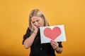 Upset woman holds piece of paper with red heart regretfully she put head in hand