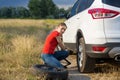 Young upset woman lifting her broken car with jack to change flat tyre on countryside road Royalty Free Stock Photo